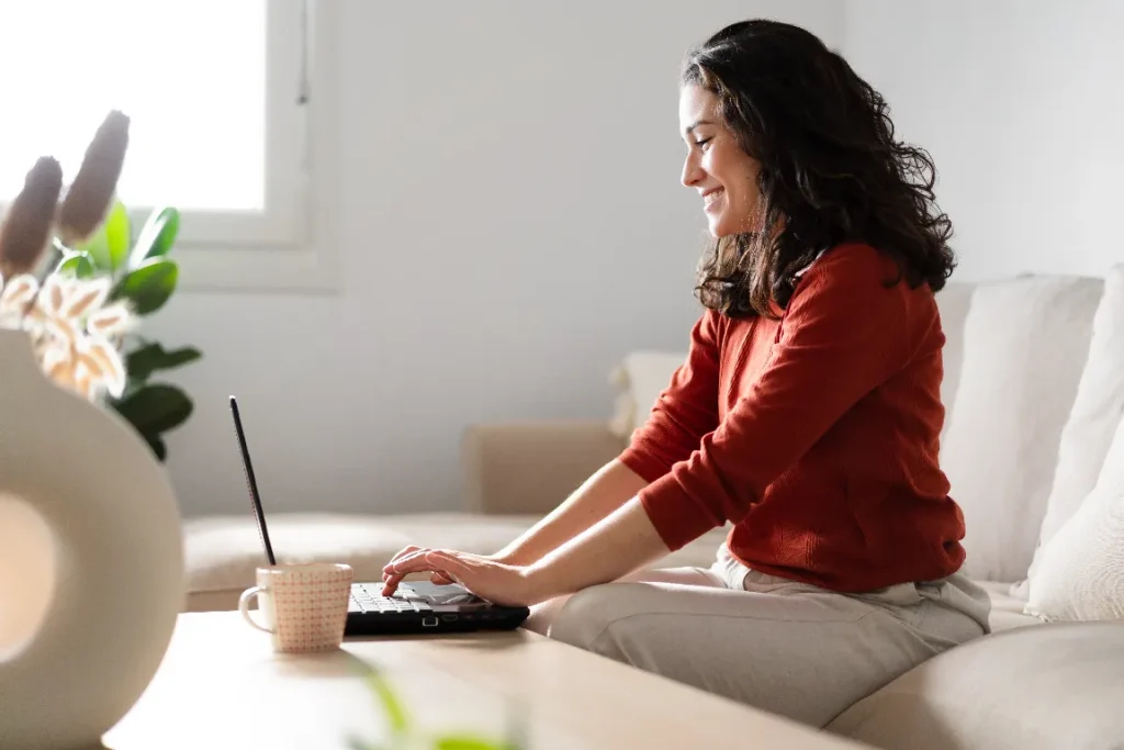 Smiling woman sitting on a couch using a laptop to complete online dental appointment forms for Pearl Dental.